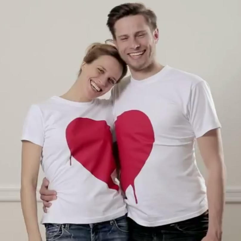 A couple standing close with their t-shirts forming a heart.